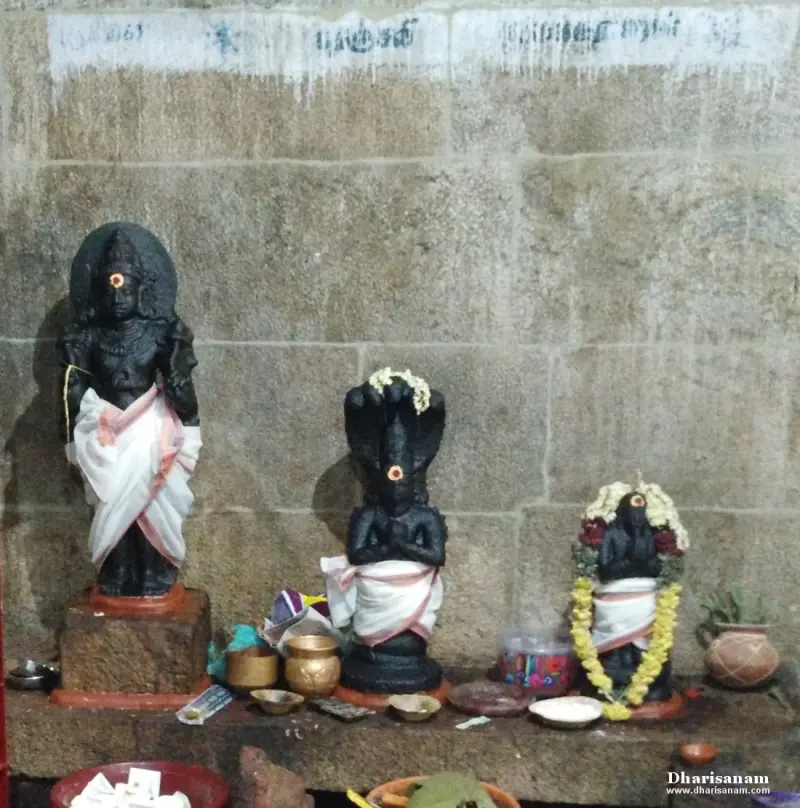 Three dark images in white cloth before a stone wall, the middle one with a five-hooded cobra overhead