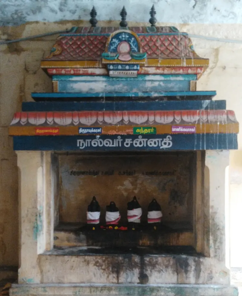 Four small dark idols in white cloths inside a painted shrine
