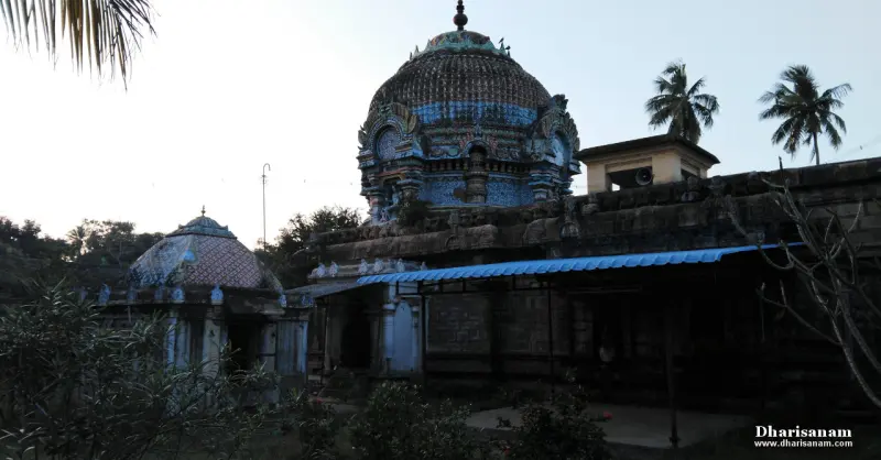 Domed sanctum tower in blue and brown above a stone wall, with a blue roof porch and palm trees