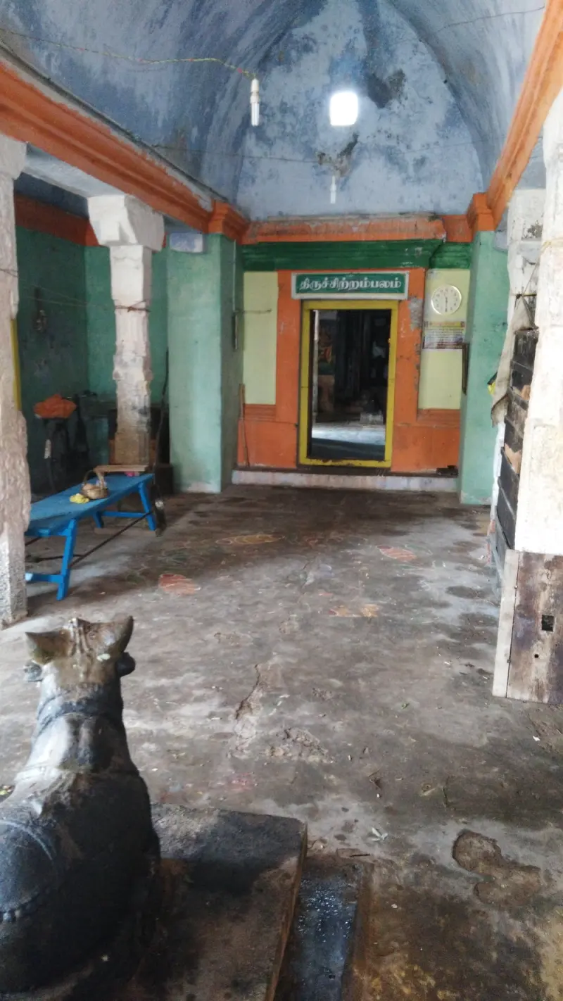 A vaulted hall with a stone Nandi in the foreground and a lit doorway at the far end