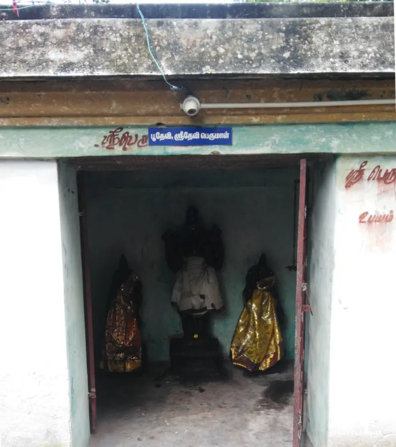 A small shrine with a dark central idol and two robed figures at its sides; a blue board names Bhoodevi and Sridevi.
