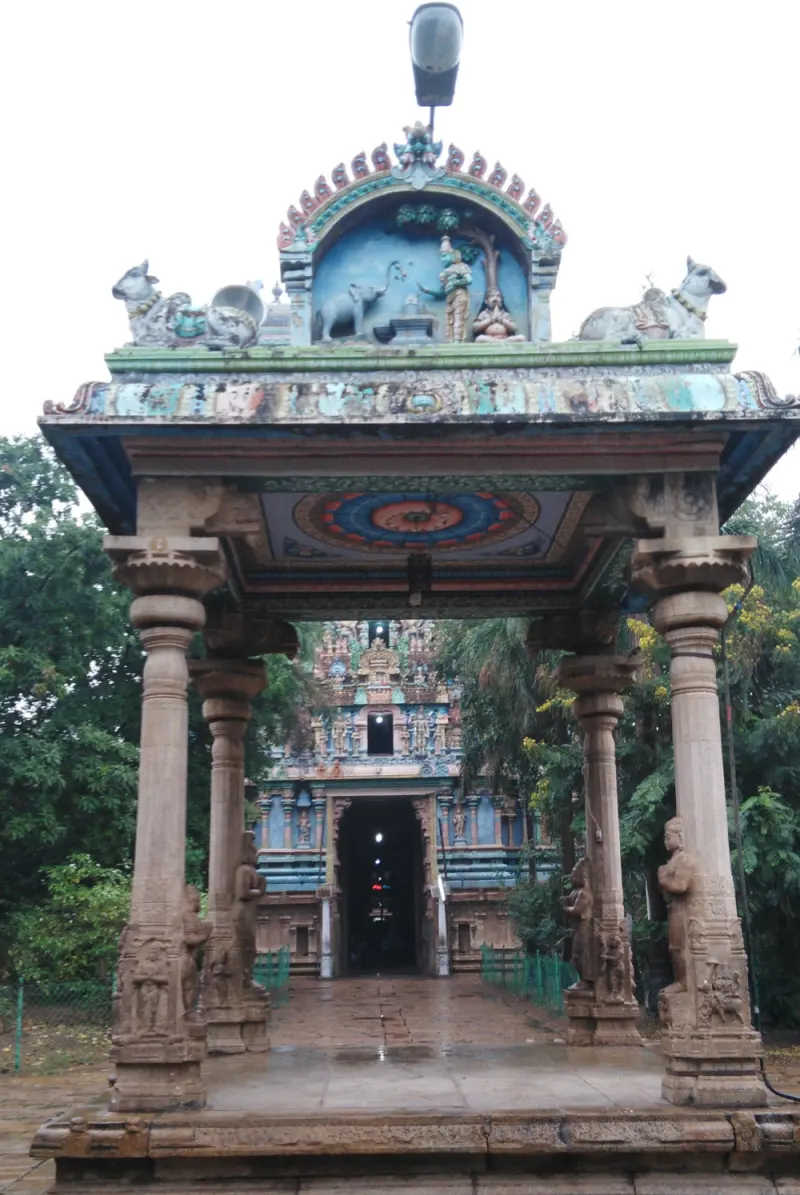 A stone porch with carved pillars frames a doorway leading to a shrine with a colourful roof.