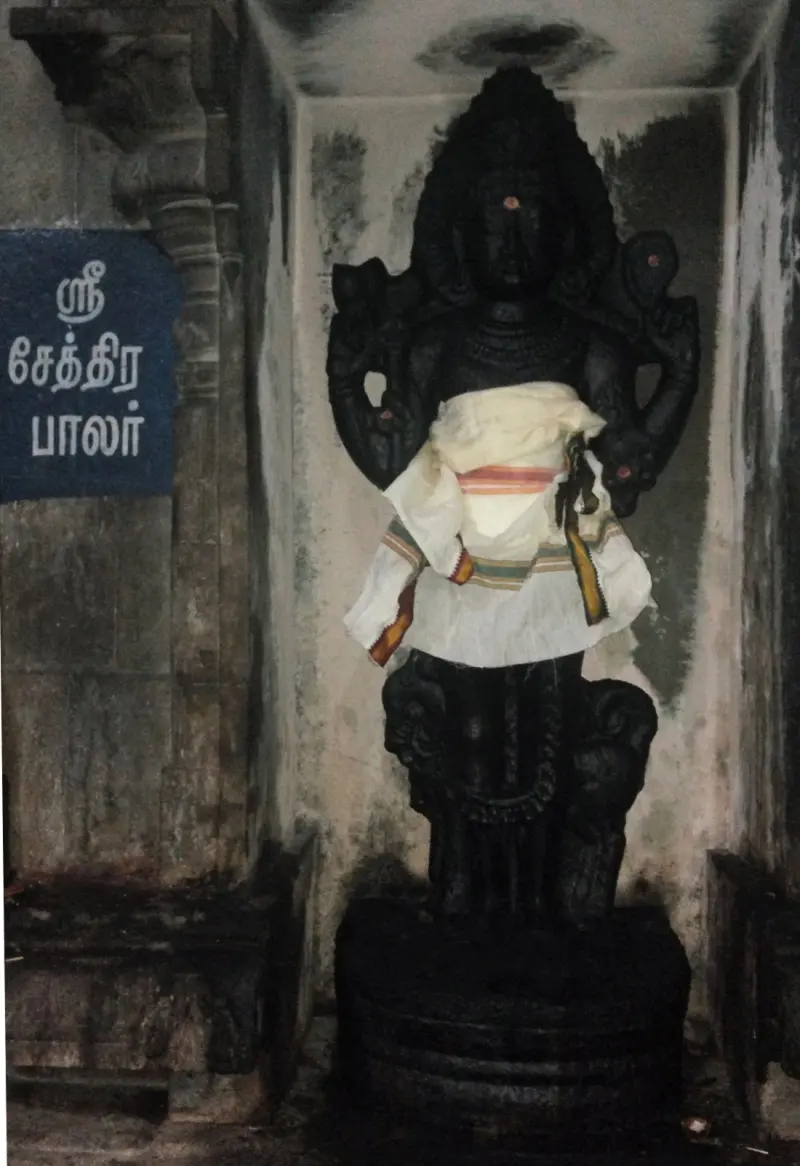 A dark standing figure in a niche in a white and cream cloth, beside a name board