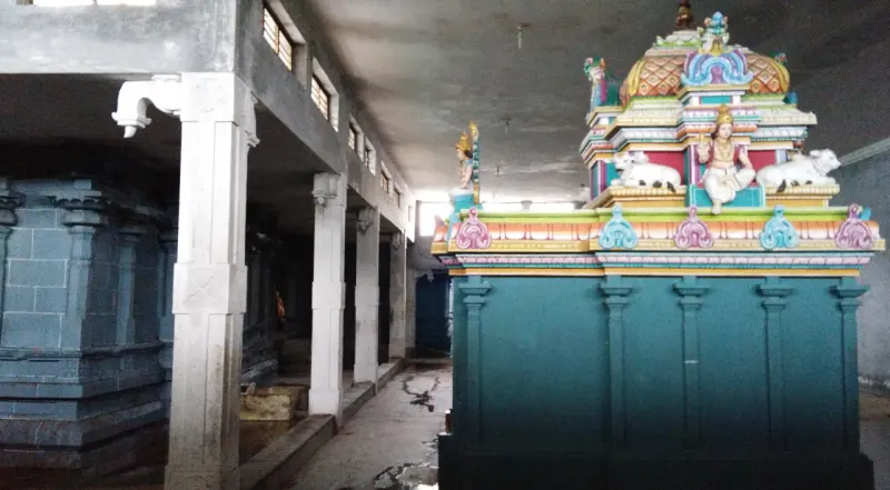 A covered stone corridor with white pillars; on the right, a teal shrine with a colourful tower topped by bull figures.
