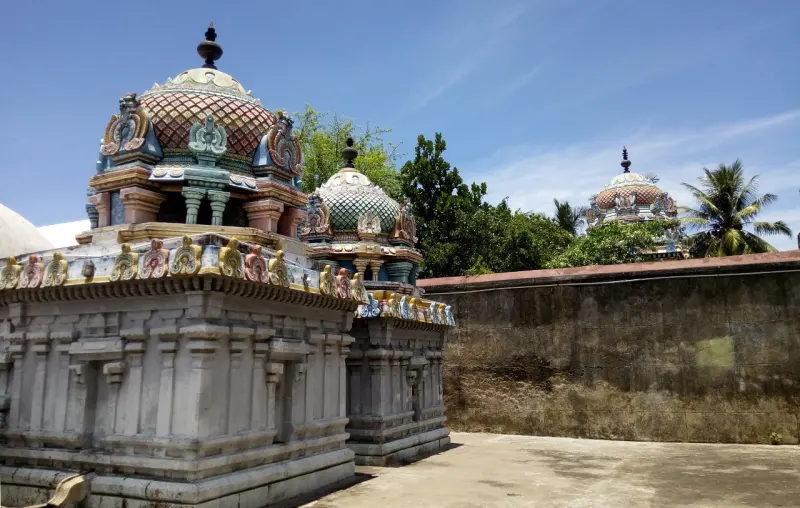 Two small painted domed towers rising above stone shrine walls, with a larger tower in the distance