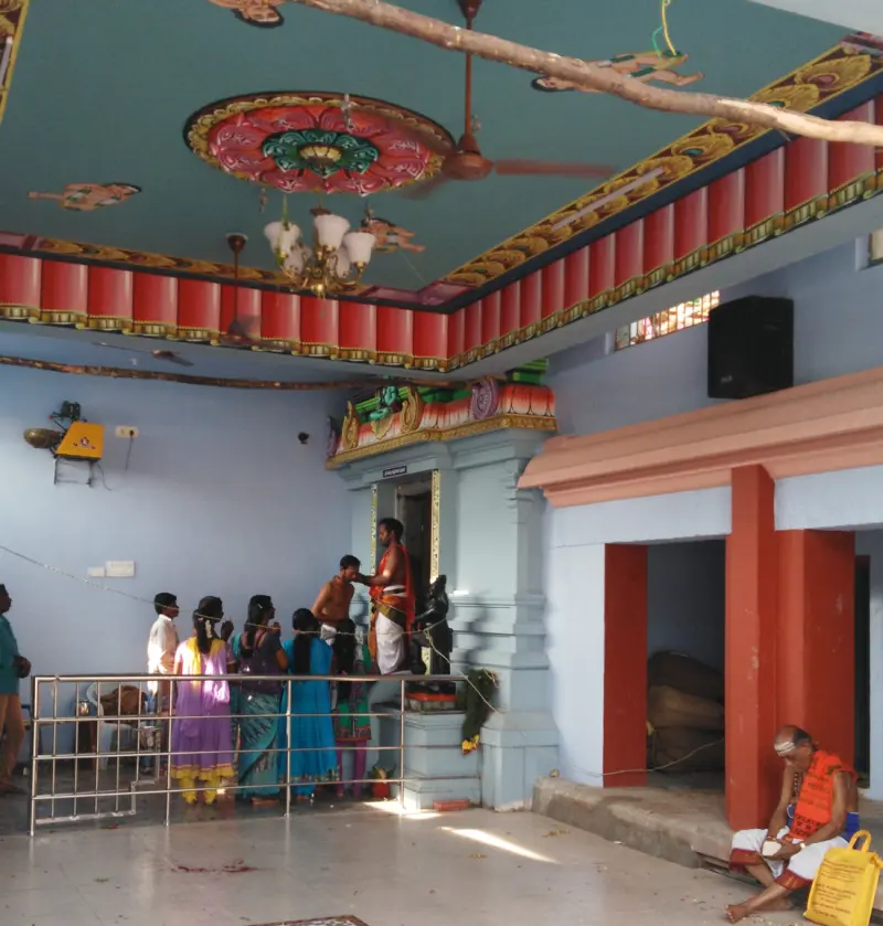 Devotees before a shrine doorway while a priest gives prasadam