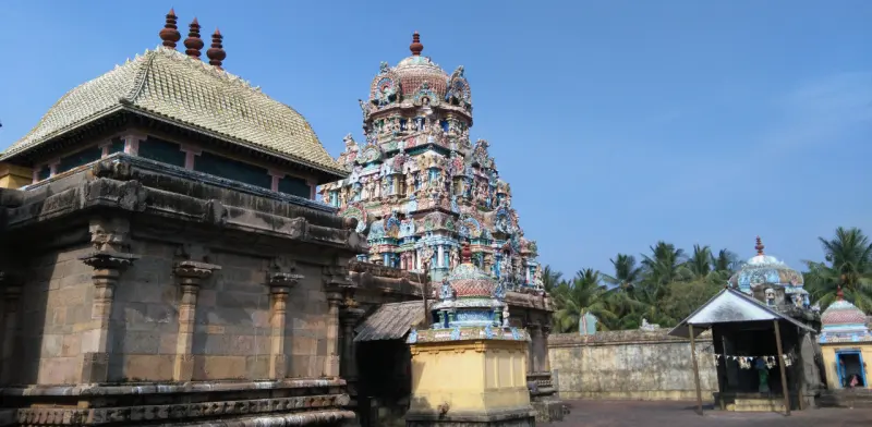 A mandapam with a tiled roof on the left, the main tower at the centre and palm trees beyond the wall