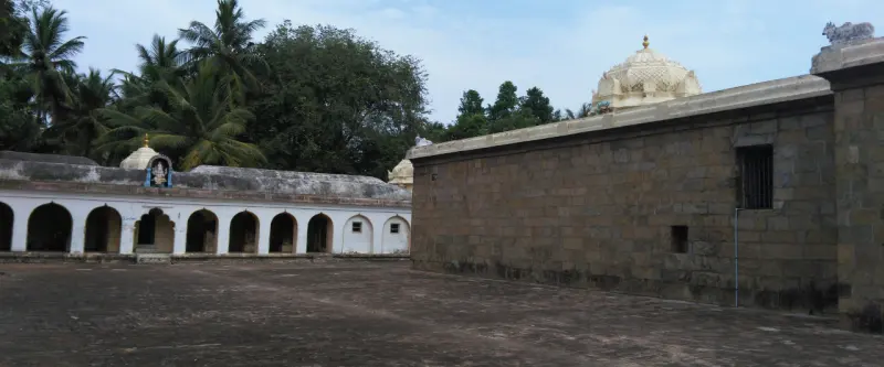 A stone wall on the right, with a white arched corridor on the left across the courtyard