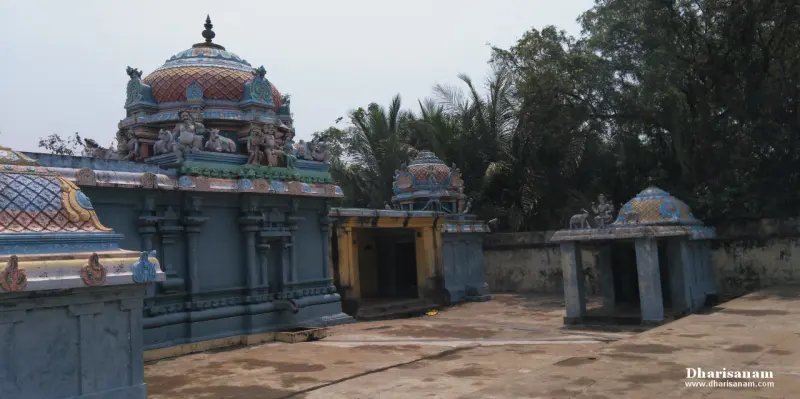 A paved courtyard with domed blue shrines and a small open pavilion, trees behind the wall