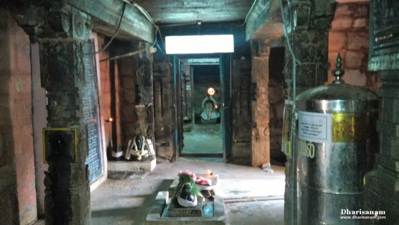 A dim stone corridor with a small decorated shrine in front and a lit doorway beyond.