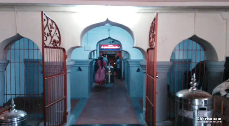 Arched openings with iron gates leading to a lit shrine, with a woman in a pink saree walking in