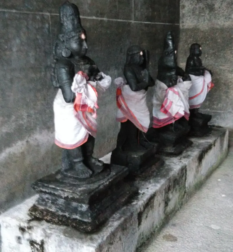 Four small dark stone figures in white and red cloths on a stone ledge