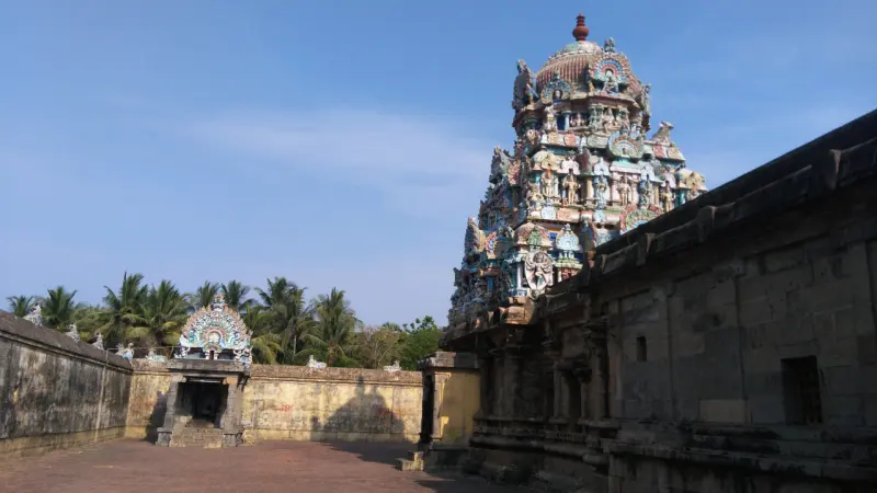 A painted tower rises behind a long stone wall, with a small shrine across the open courtyard