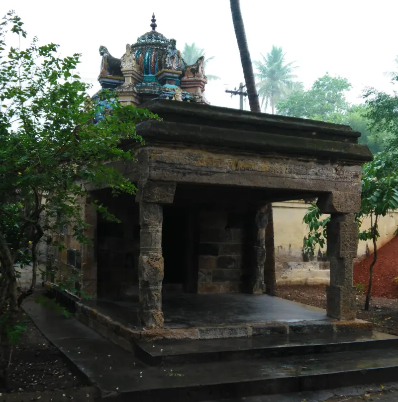 An open stone shrine with a small colourful tower above it, among trees.