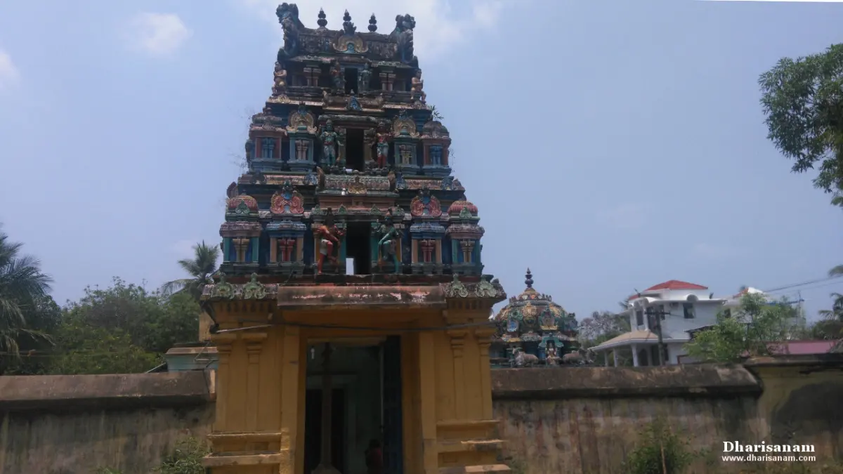 A three-tiered tower of painted sculptures over a yellow gateway, with the compound wall alongside.