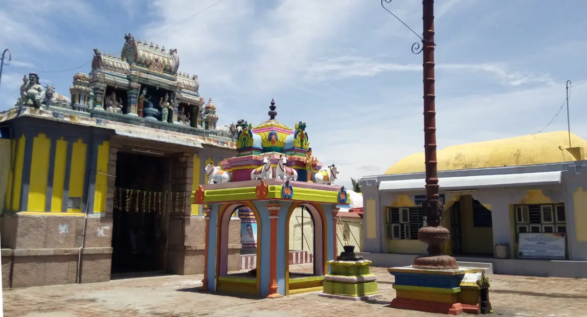 Open courtyard with a tall flagstaff, a small painted shrine and a tower on the left