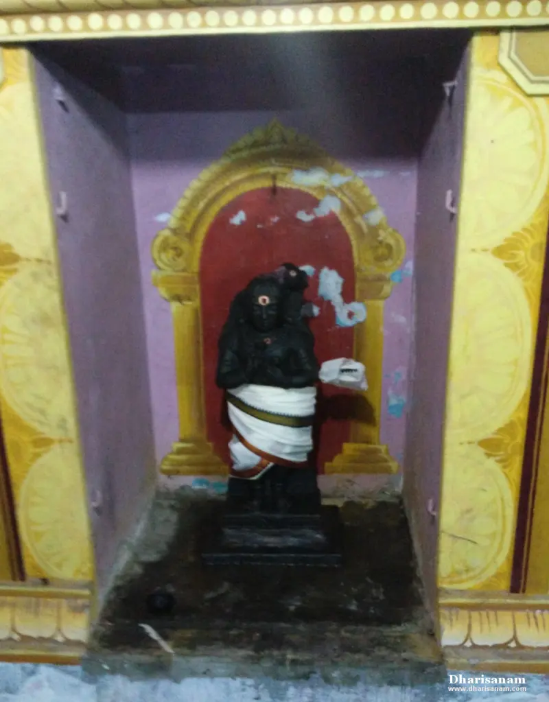 A black stone figure with joined hands in a white cloth, standing in a painted niche