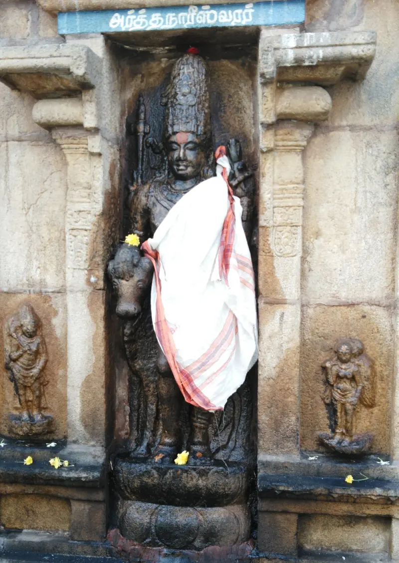 Standing stone figure beside a bull, wrapped in a white cloth, in a wall niche under a name board