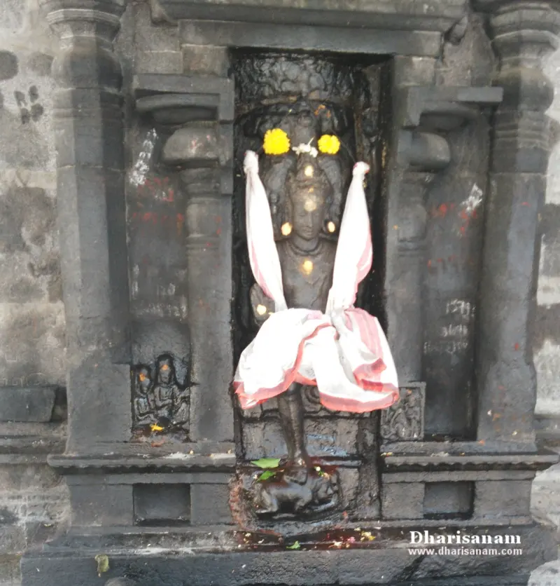 Dark stone idol in a niche, with yellow flowers on its head and a white and red cloth