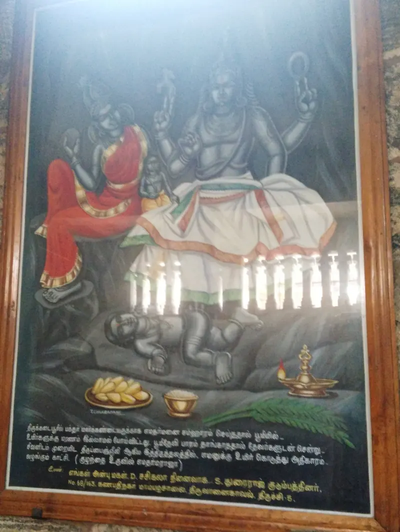 A framed painting of Shiva and Parvathi seated, a child lying under his feet, with a Tamil caption below.