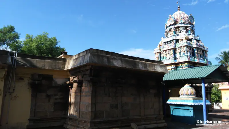A flat stone-roofed building in the foreground, a colourful tower behind it and a small shrine under a green roof