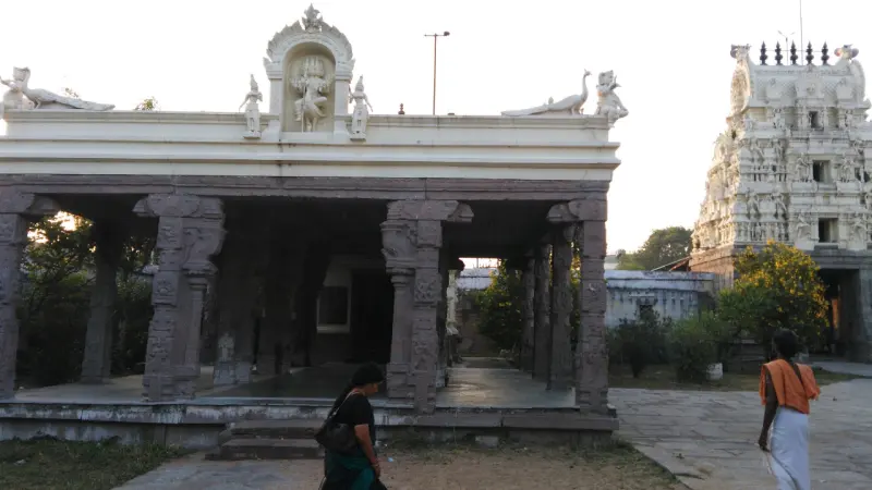 A carved stone hall with rooftop sculptures, a white tower beyond
