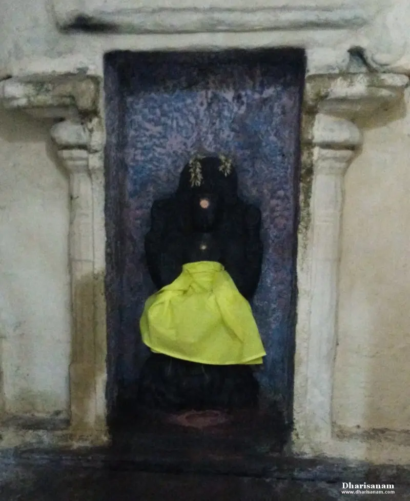 A dark stone idol in a recessed niche, covered at the waist with a bright yellow cloth.