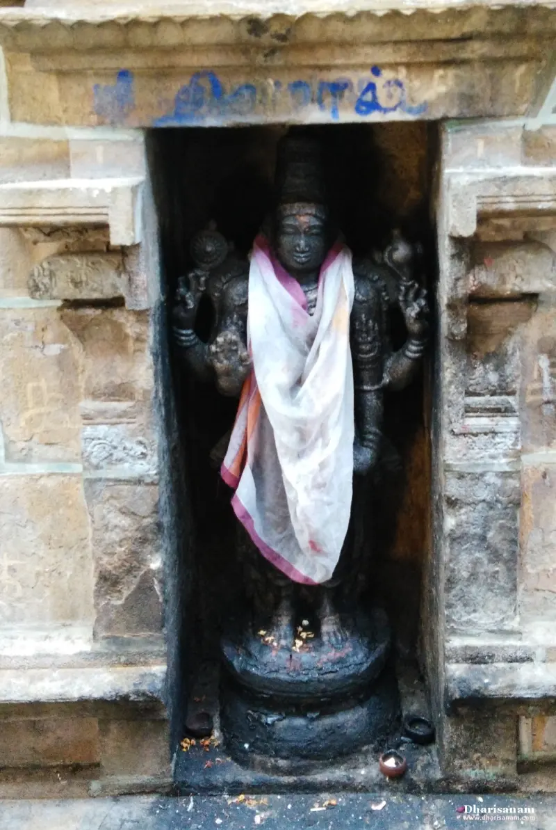 A standing dark stone idol with four arms, wearing a white and pink cloth, in a stone niche