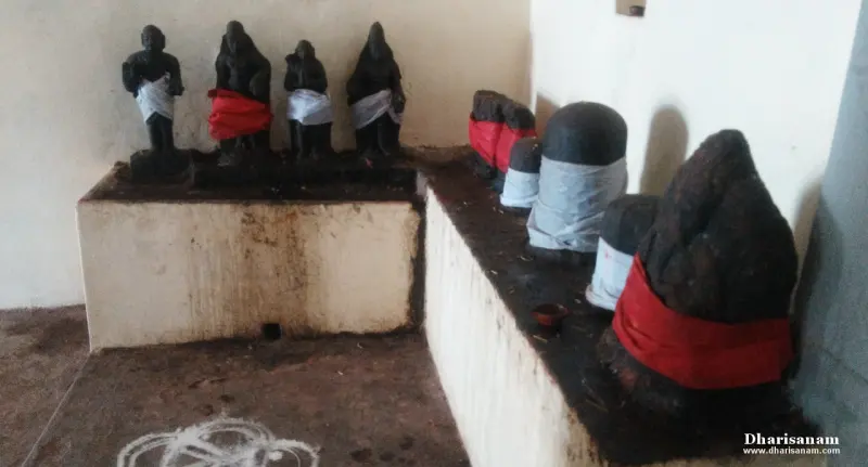 Four small black idols in white and red cloth on a platform, with several Shivalingams in cloth wraps beside them