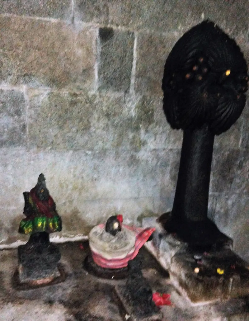 Black stone palm tree carving with two small painted deity statues beside it