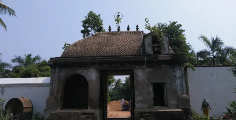 A weathered stone entrance arch with a tiled barrel roof, set in a white compound wall