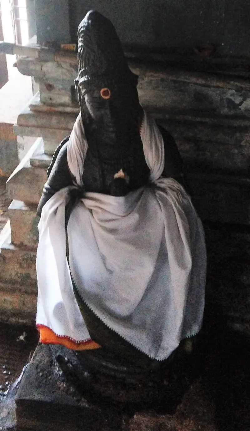 A black stone Vinayakar idol with a red mark on its forehead, wrapped in white cloth with an orange edge.