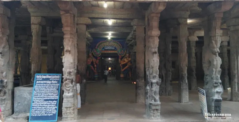 A long hall of carved stone pillars with an information board and a lit shrine entrance at the far end