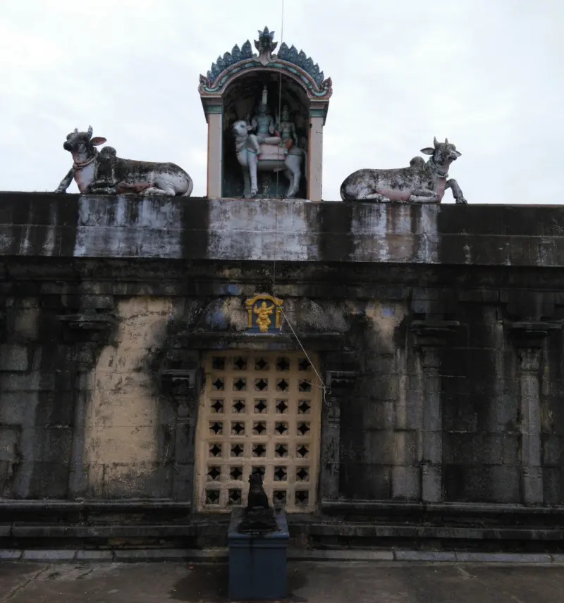 A stone wall with a latticed window, a small image above it, and two seated bulls flanking a painted niche on top.