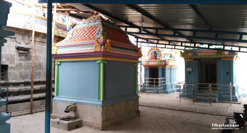 Small blue shrines with painted roofs under a metal roof, beside a stone wall at the left