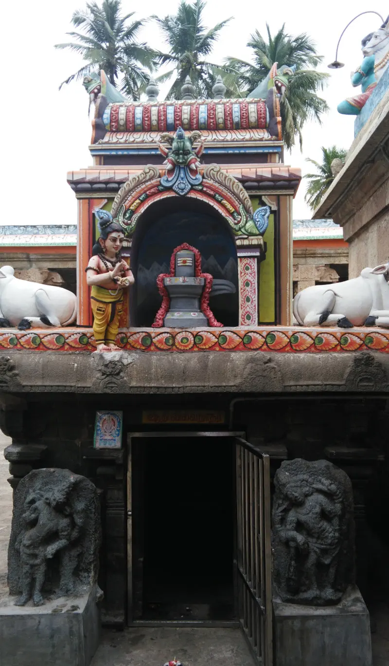 A shrine with a garlanded lingam in an arch, a painted figure beside it, and two stone figures at the door
