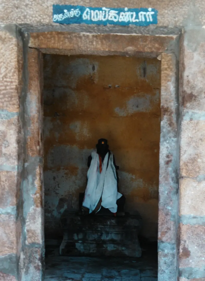 A small stone doorway with a Tamil name board above it; inside, a dark idol draped in white cloth.