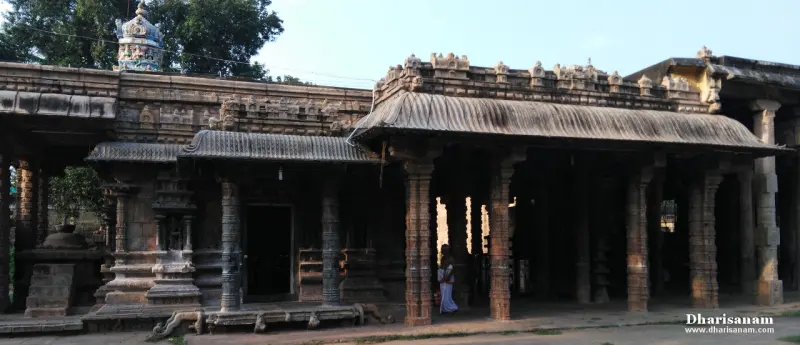 A long stone hall with carved pillars and a sloping tiled roof, a person standing in the shade