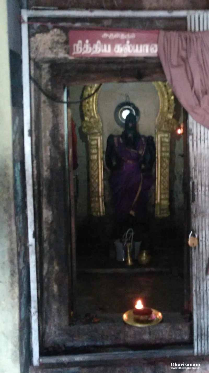 Idol in a purple sari between gilded arches, with a lit lamp in front