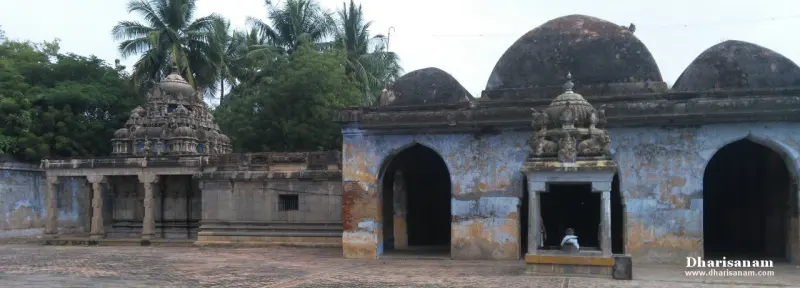 A paved courtyard with weathered domed halls at right and a small sculpted shrine tower at left