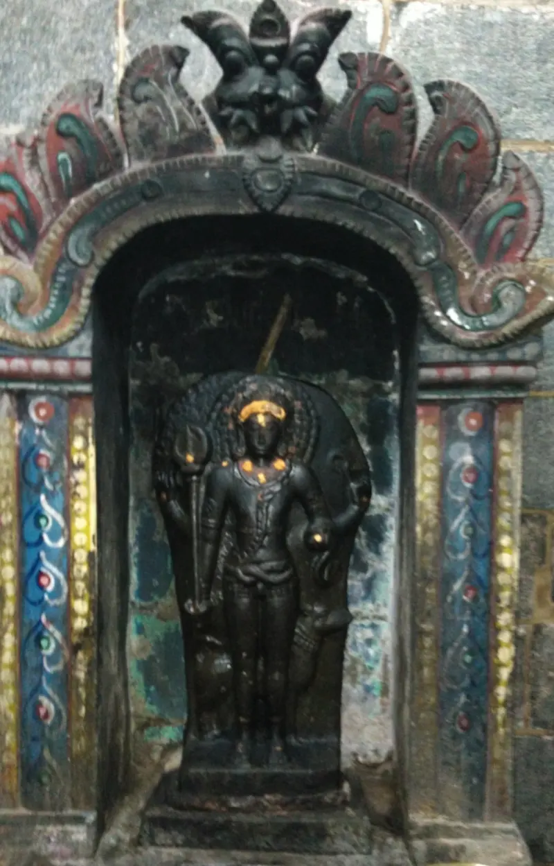 A dark standing figure holding a staff, set in a niche with a painted arch.