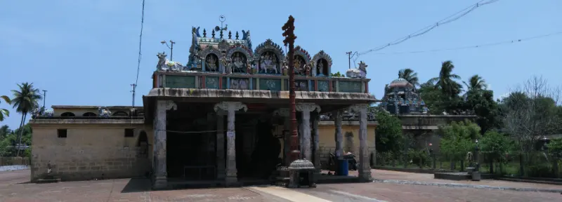 A pillared porch with a decorated roof and a wooden flagstaff in front