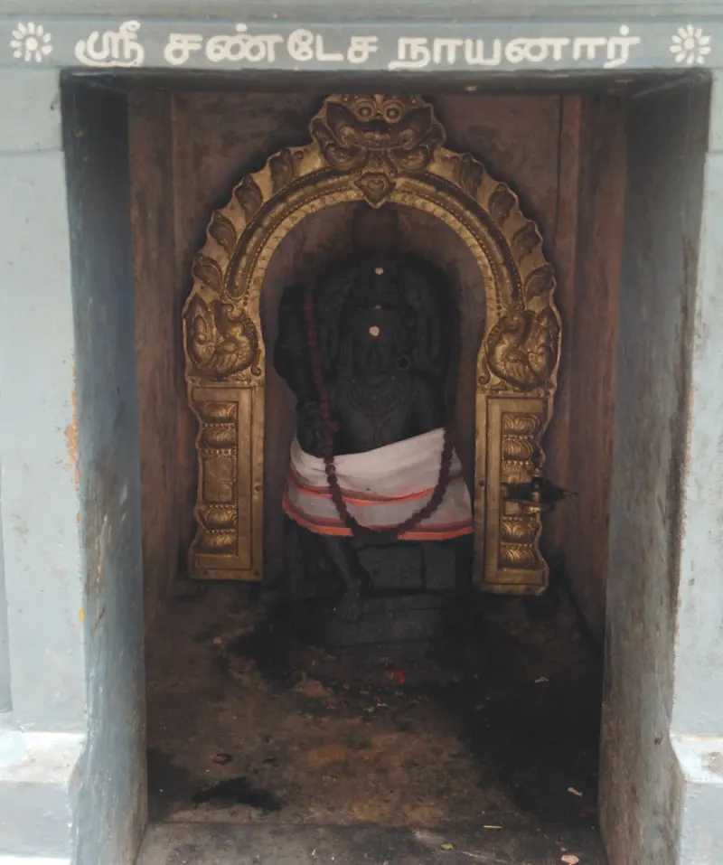 Black Chandikeswarar idol with a gold frame in a niche
