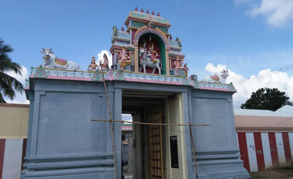 A grey gateway topped by a stucco shrine and white bulls, with its wooden door open