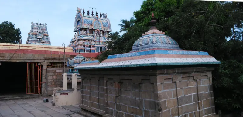 A domed stone shrine in the foreground with two painted towers behind and the corridor on the left