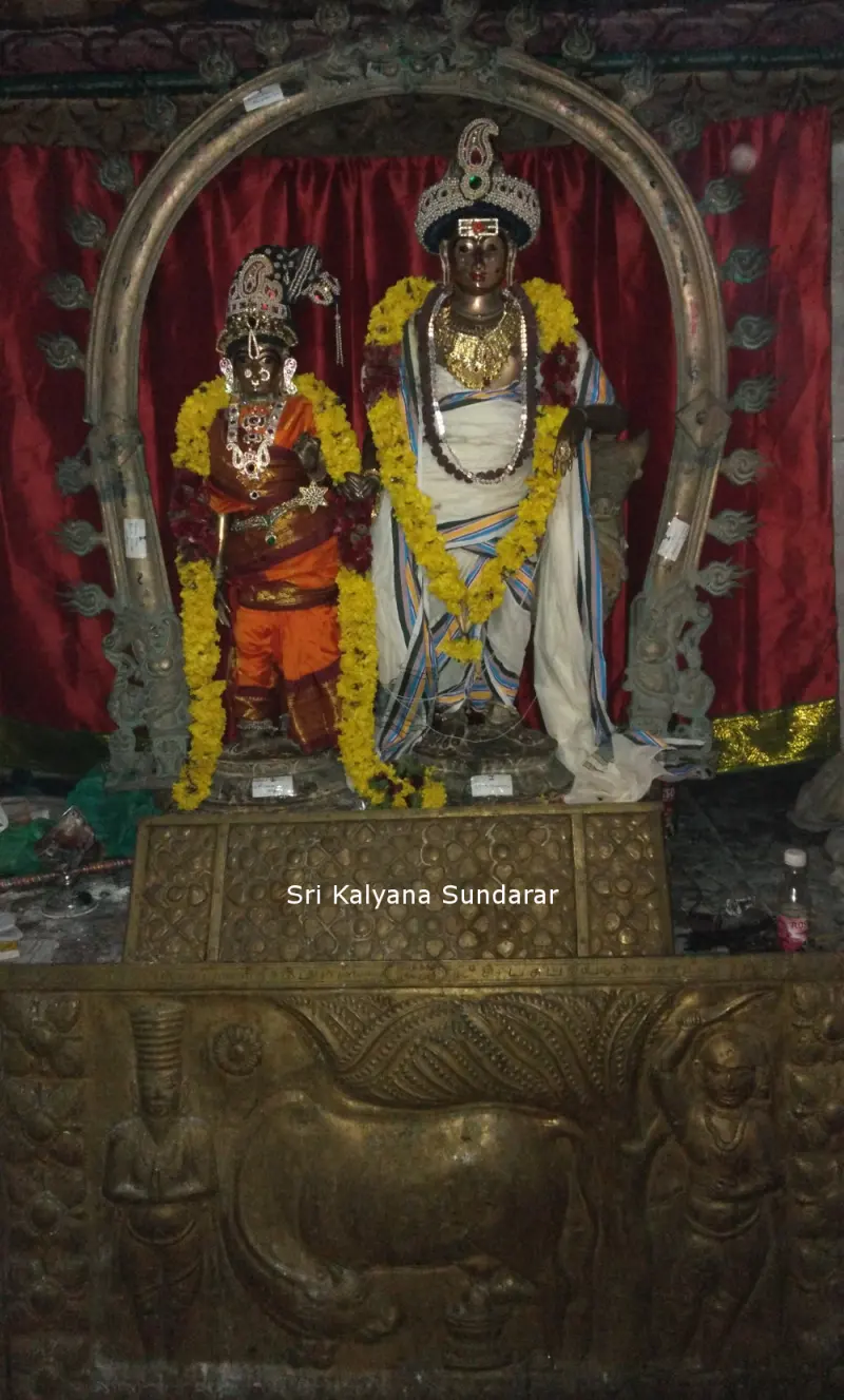 Two garlanded deities in silk clothes under a metal arch