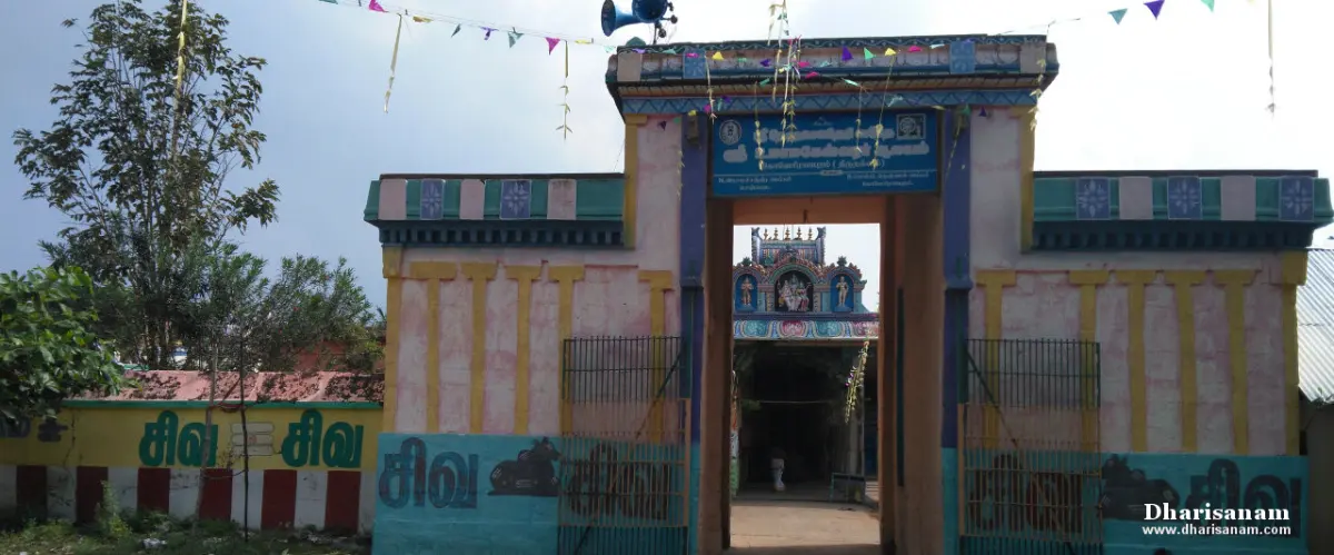 Entrance gateway with painted walls and a blue name board, a small tower visible beyond