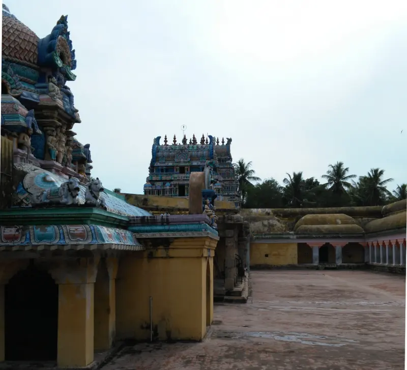 A wide stone courtyard with a coloured tower in the distance and the domed shrine roof at left.