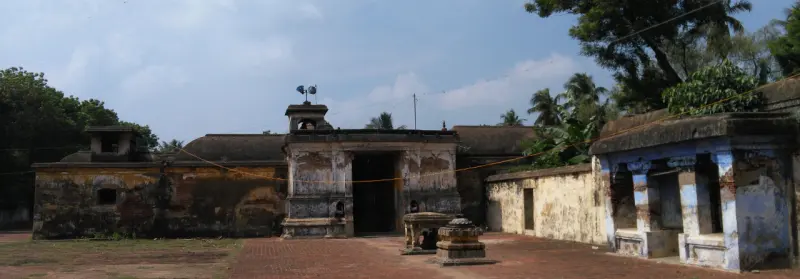 An inner gateway in a weathered wall across a brick-paved courtyard, with trees and a small shrine to the right.