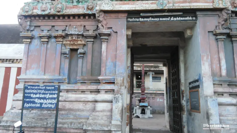 A weathered gateway with a Tamil name board above the doorway and a blue information board at left